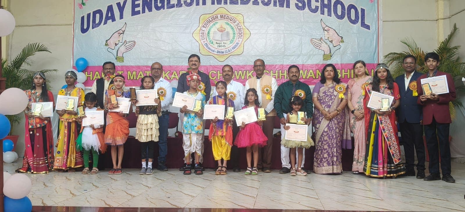 Prize winners in traditional dress holding their certificates on stage with staff and guests